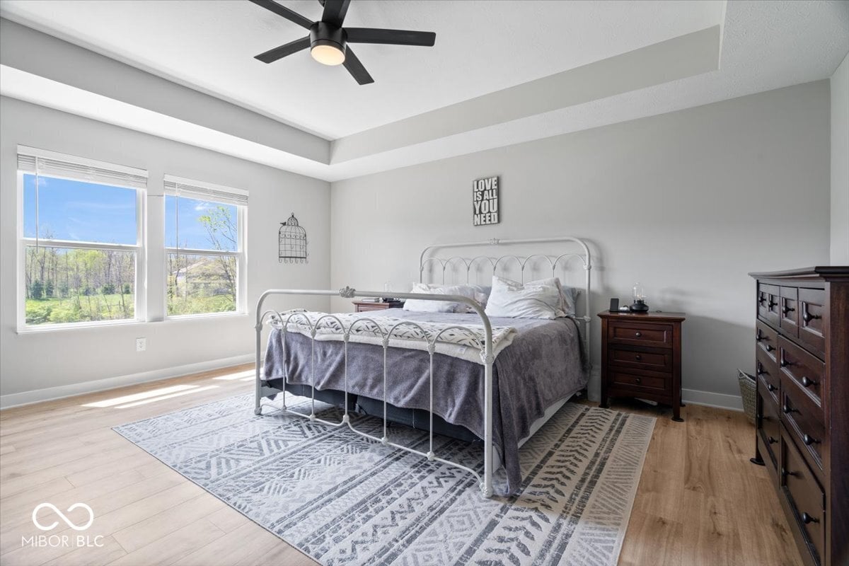 Bright primary bedroom with tray ceiling and ample windows.