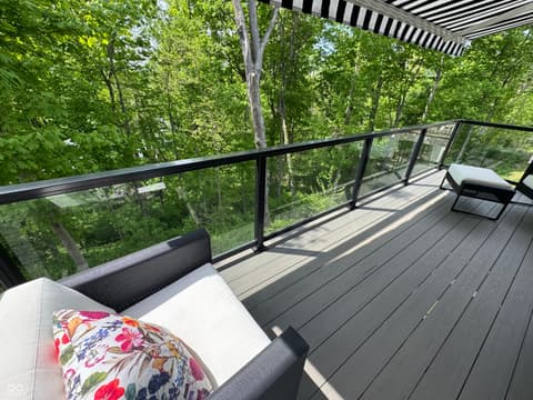 Outdoor living area at 14442 Treasure Creek Lane, Fishers, IN — Modern deck with glass railings overlooking mature forest.