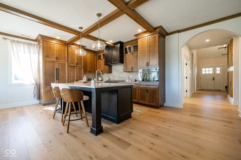Kitchen at 14565 Bedford Falls Drive, Carmel, IN — Chef's kitchen with black island and exposed beam ceiling.