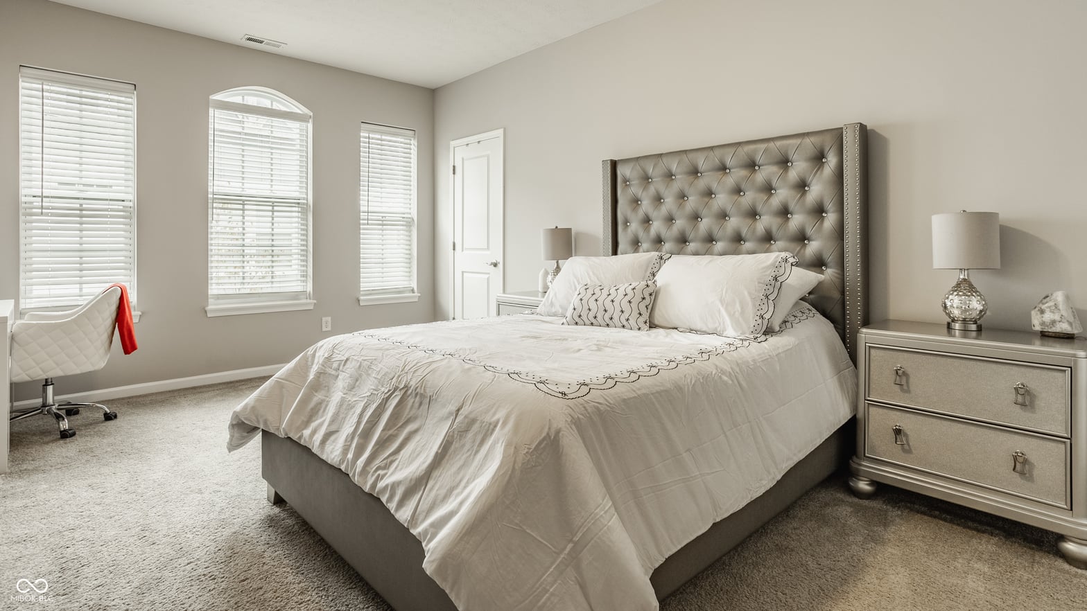Bright primary bedroom with elegant tufted headboard and natural light.