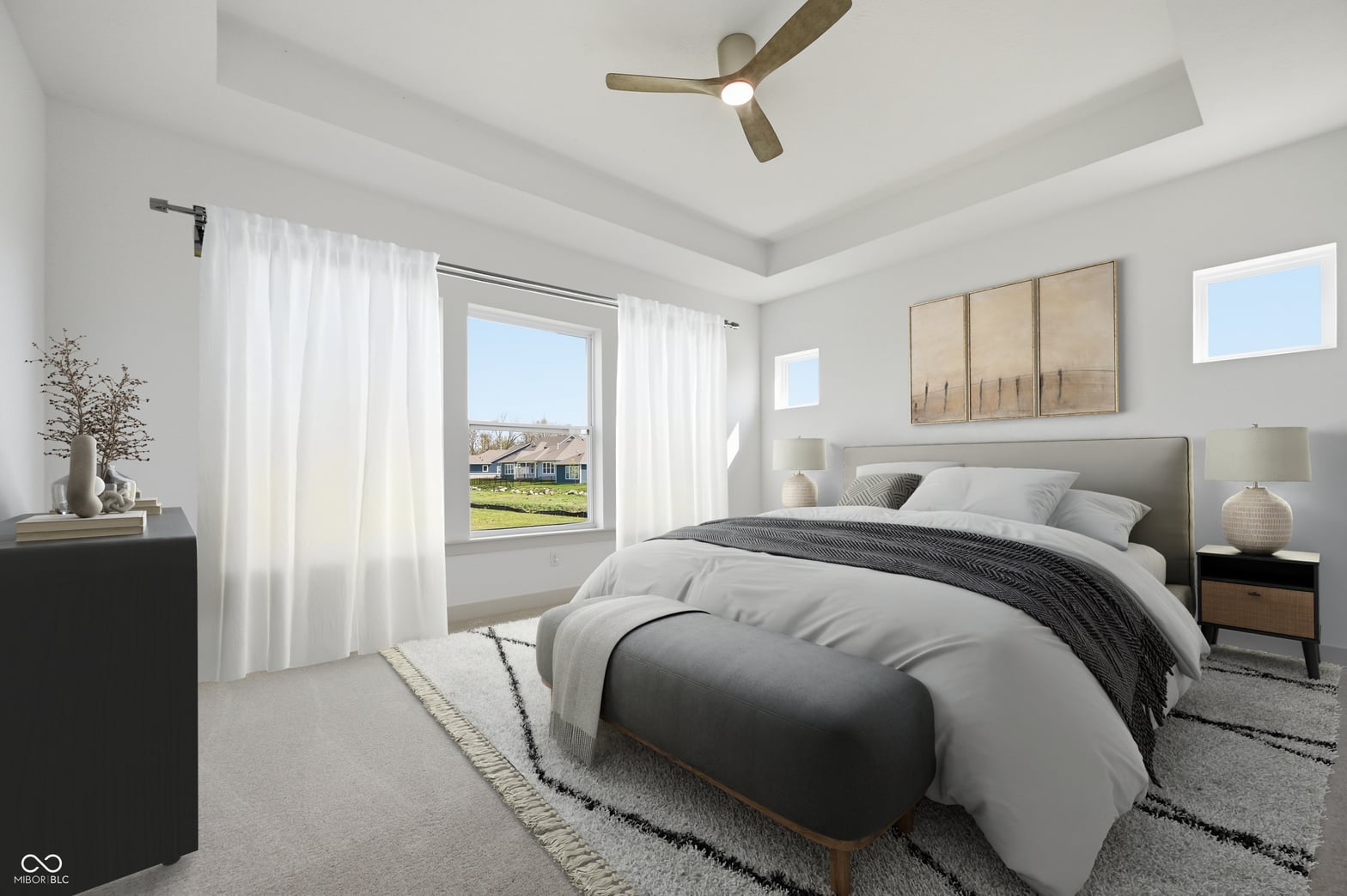 Bright primary bedroom with tray ceiling and outdoor views.