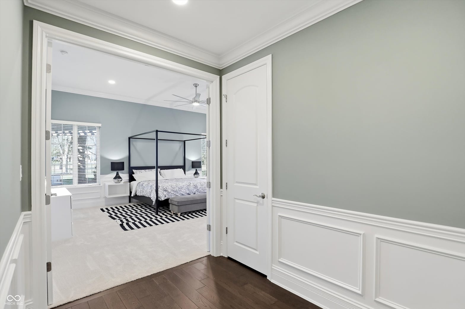 Bright primary suite with canopy bed and wainscoting.