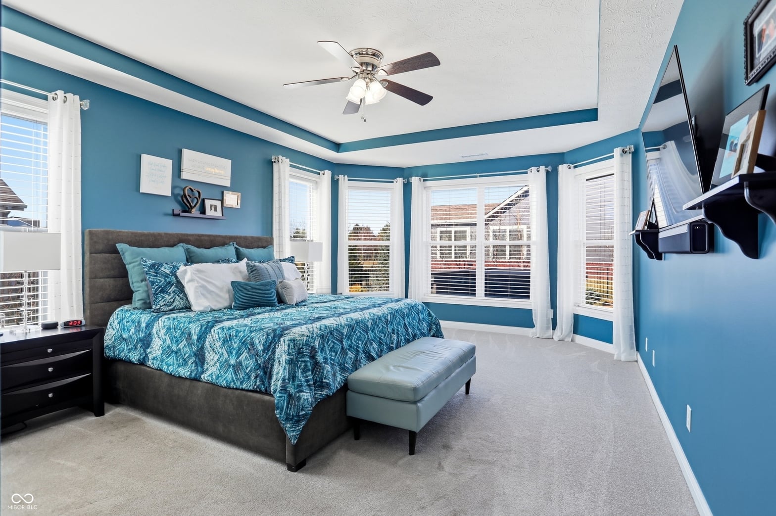 Bright primary bedroom with expansive windows and tray ceiling.
