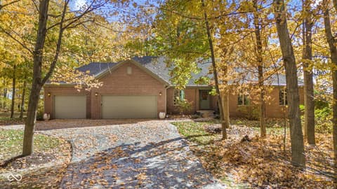 Front exterior at 10791 E State Road 47, Sheridan, IN — Brick home nestled on wooded acreage with mature trees.