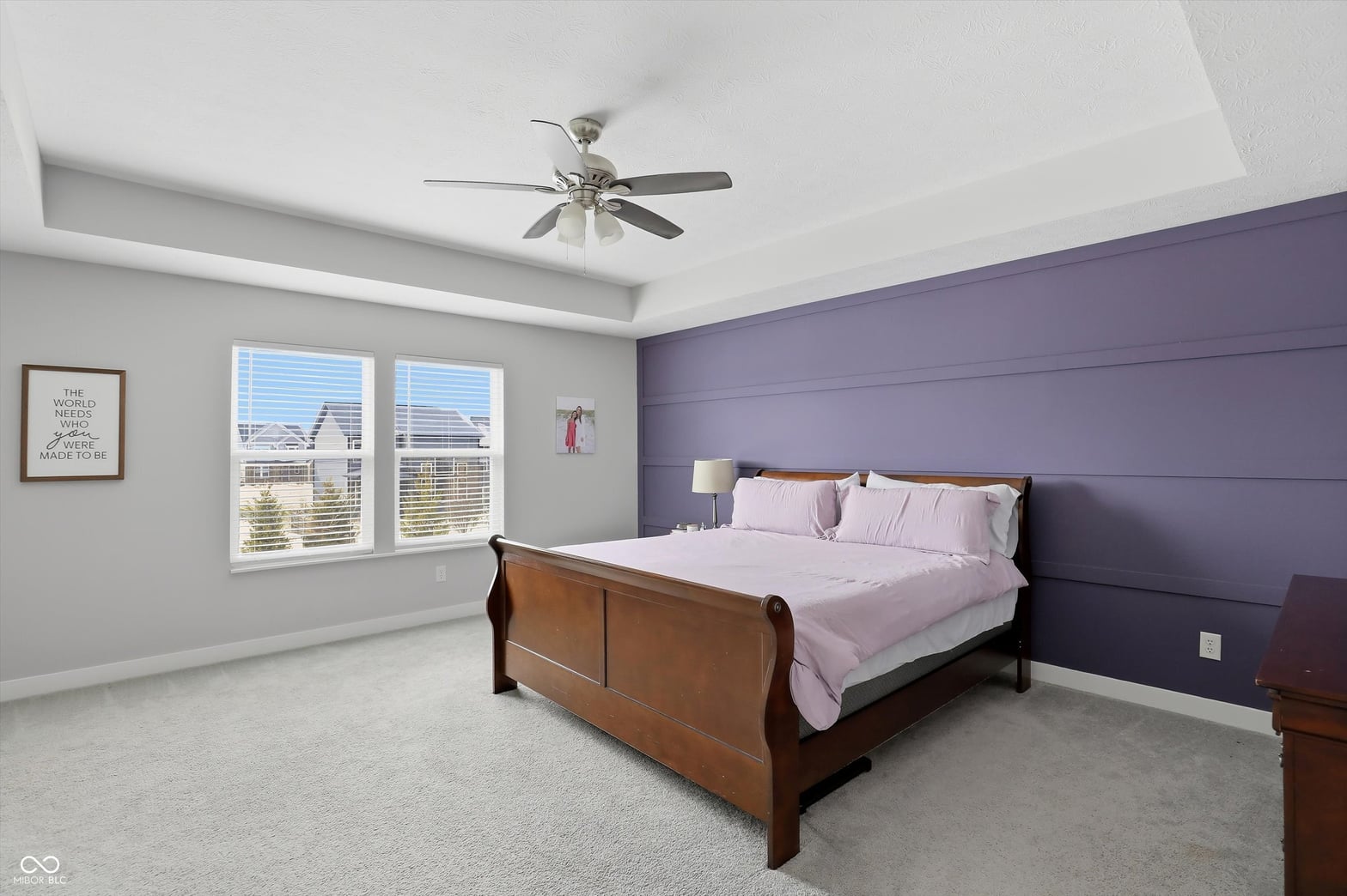 Spacious primary bedroom with purple accent wall and natural light.
