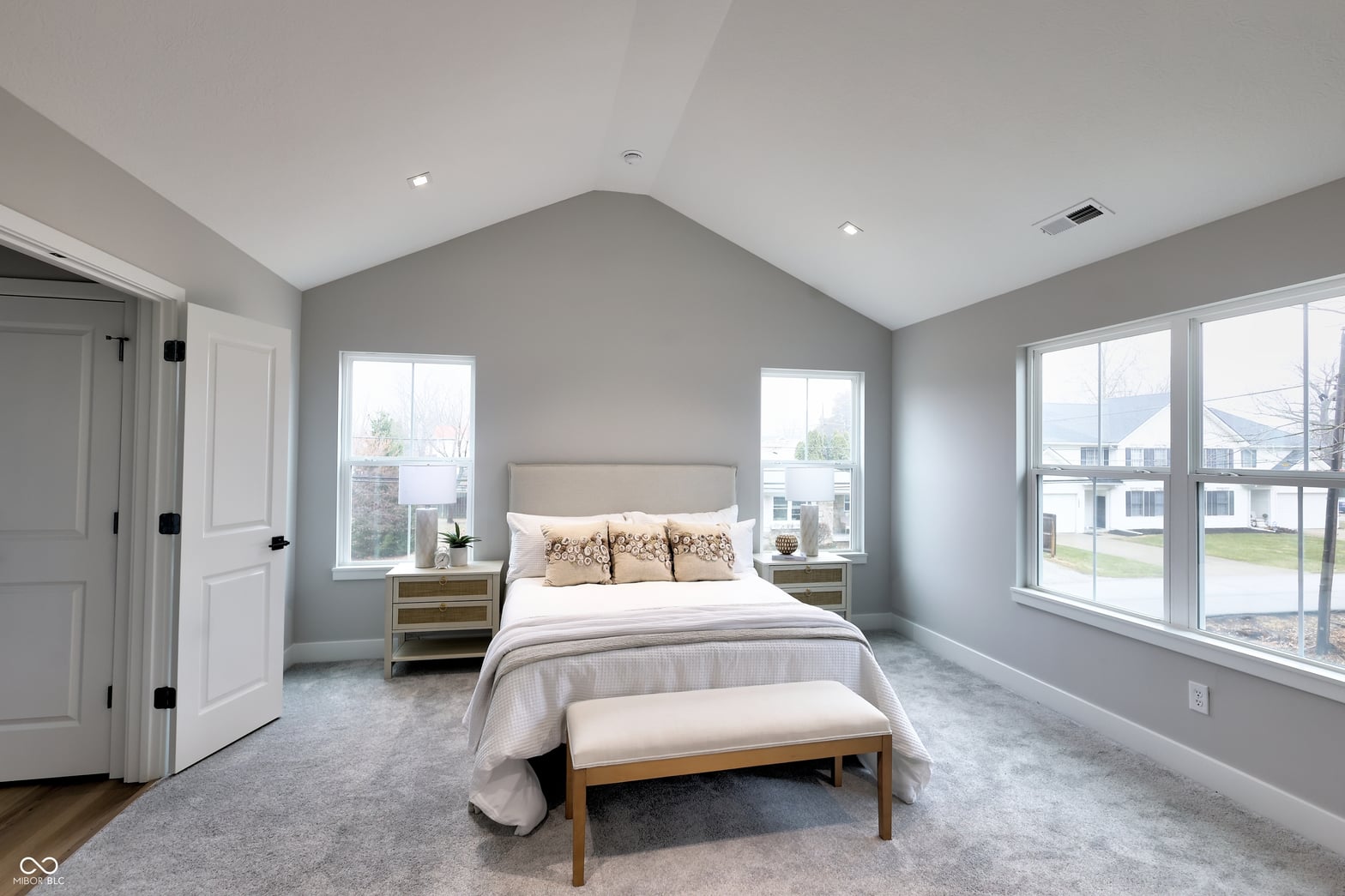 Bright primary bedroom with vaulted ceiling and multiple windows.