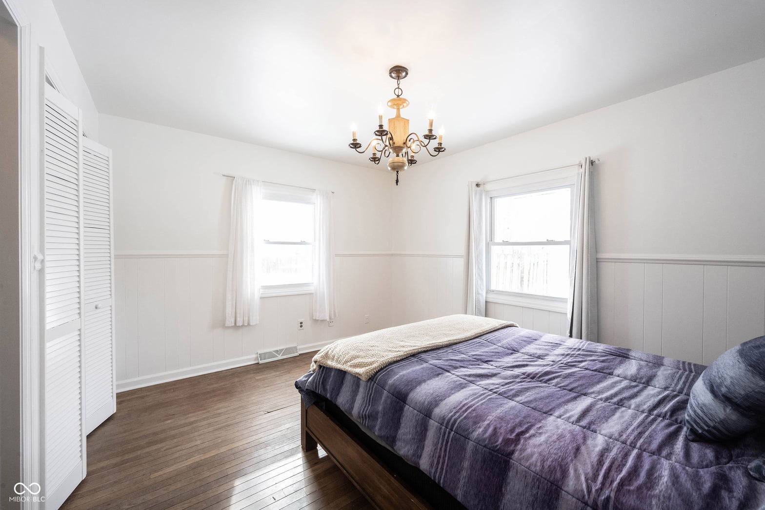 Bright primary bedroom with classic wainscoting and hardwood floors.