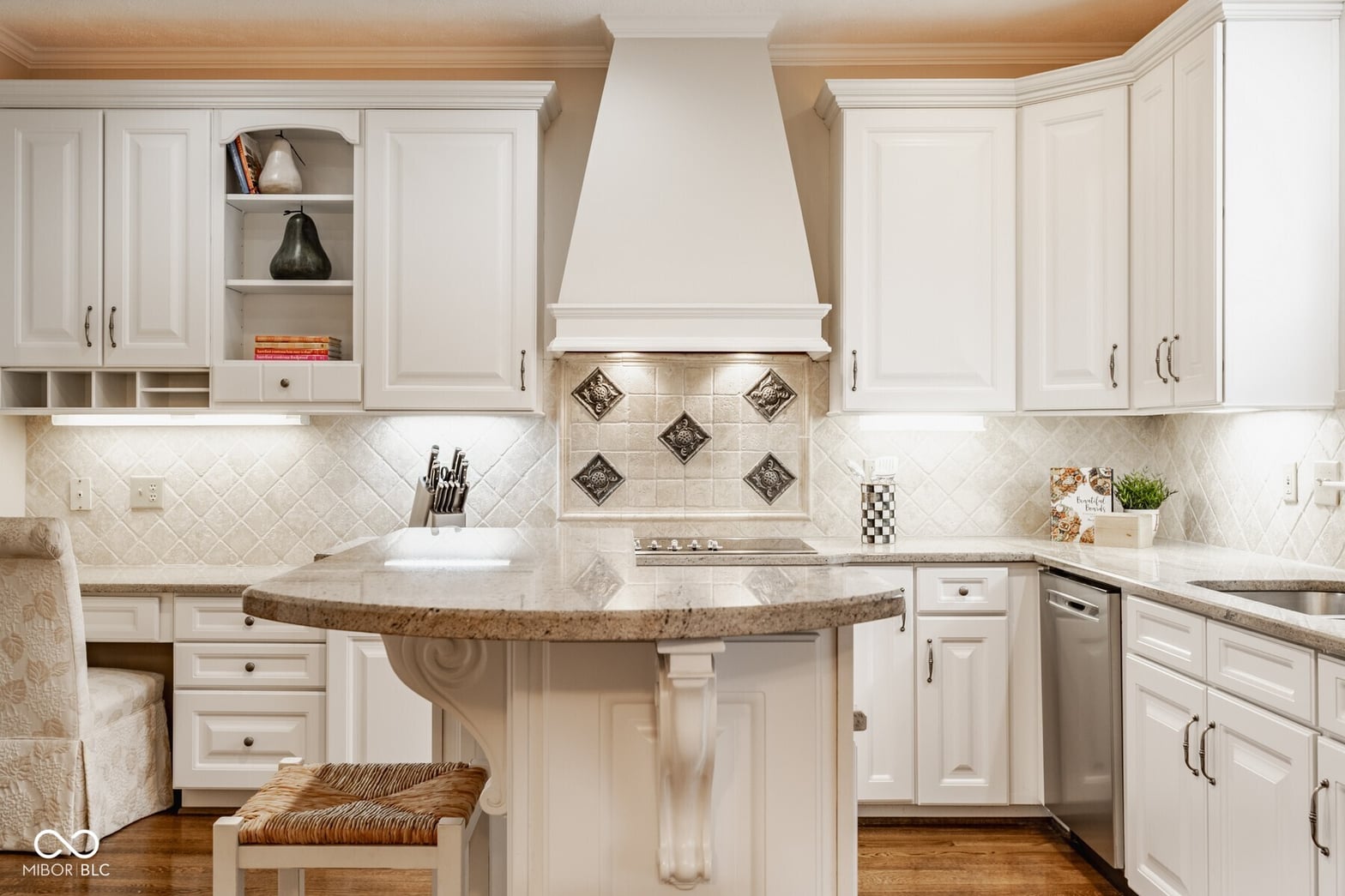 Elegant white kitchen with curved granite island and tile accents.