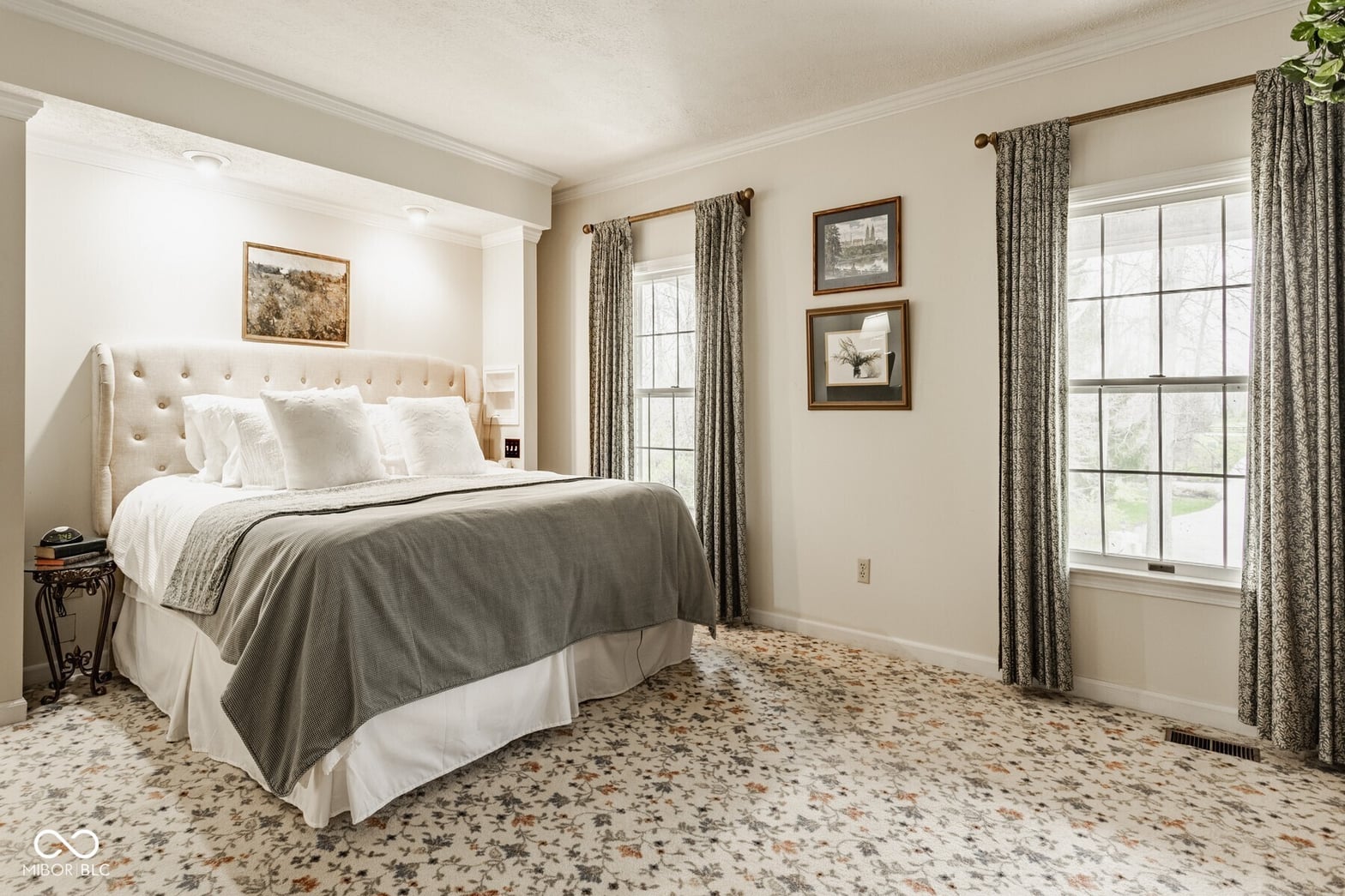 Spacious primary bedroom with luxurious tufted headboard and bright windows.