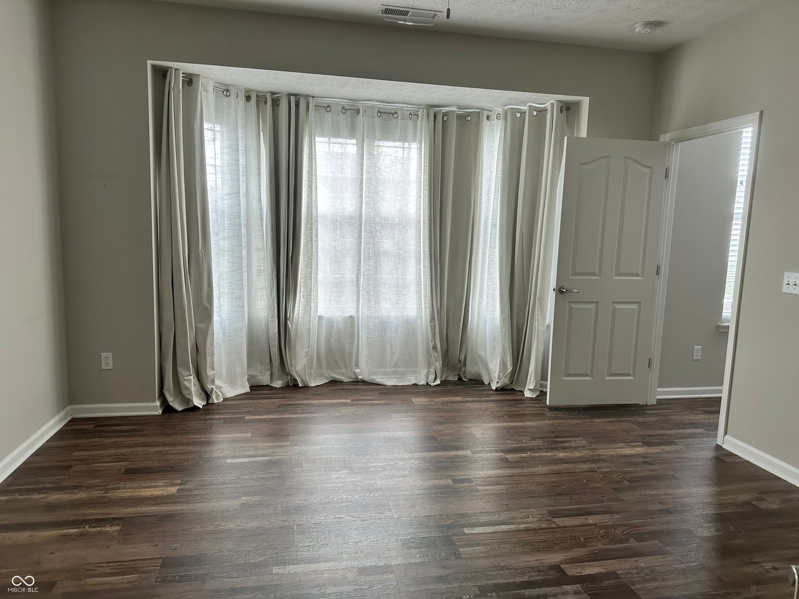 Bright primary bedroom with extensive windows and hardwood floors.