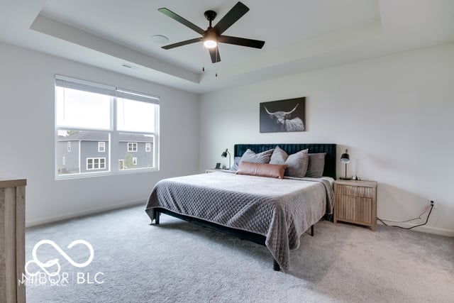 Bright primary bedroom with tray ceiling and ample windows.