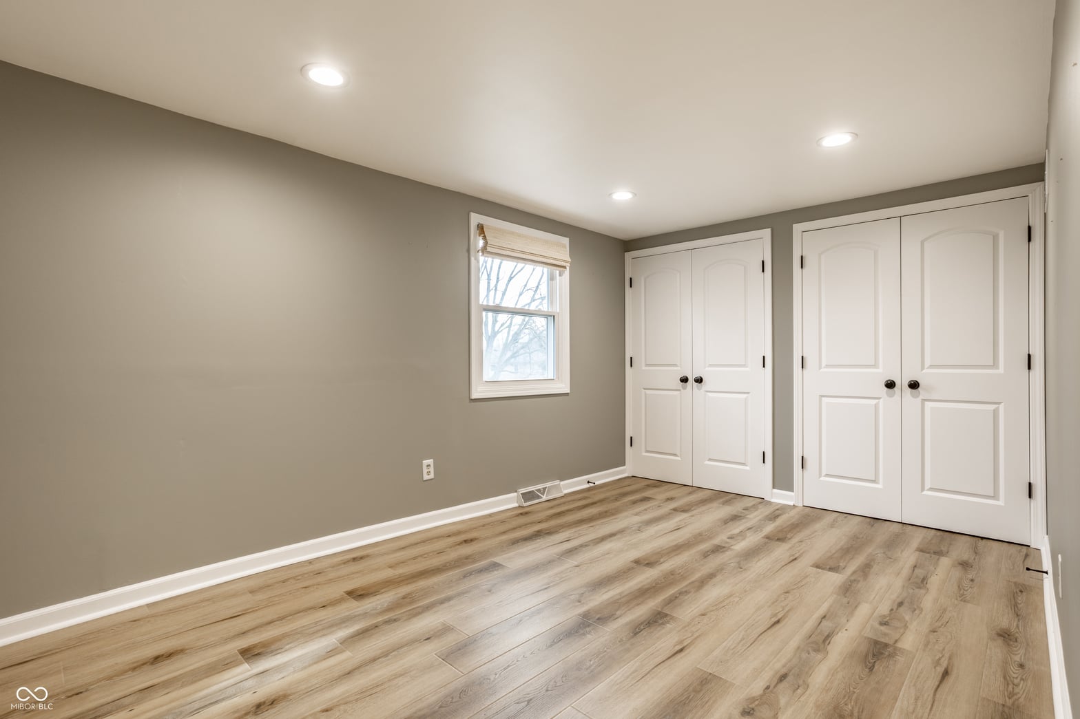 Bright primary bedroom with dual closets and hardwood floors.