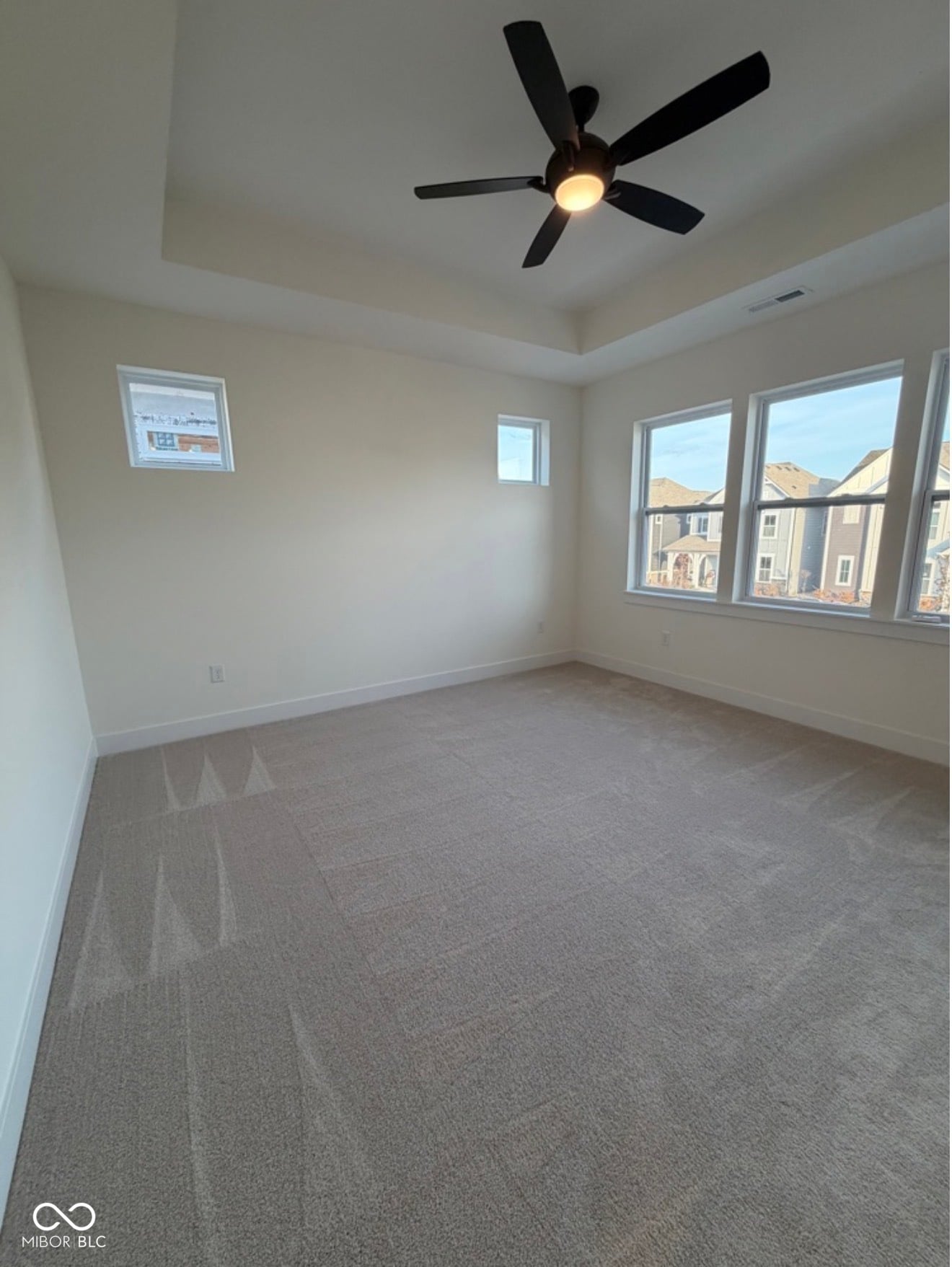 Bright primary bedroom with multiple windows and tray ceiling.