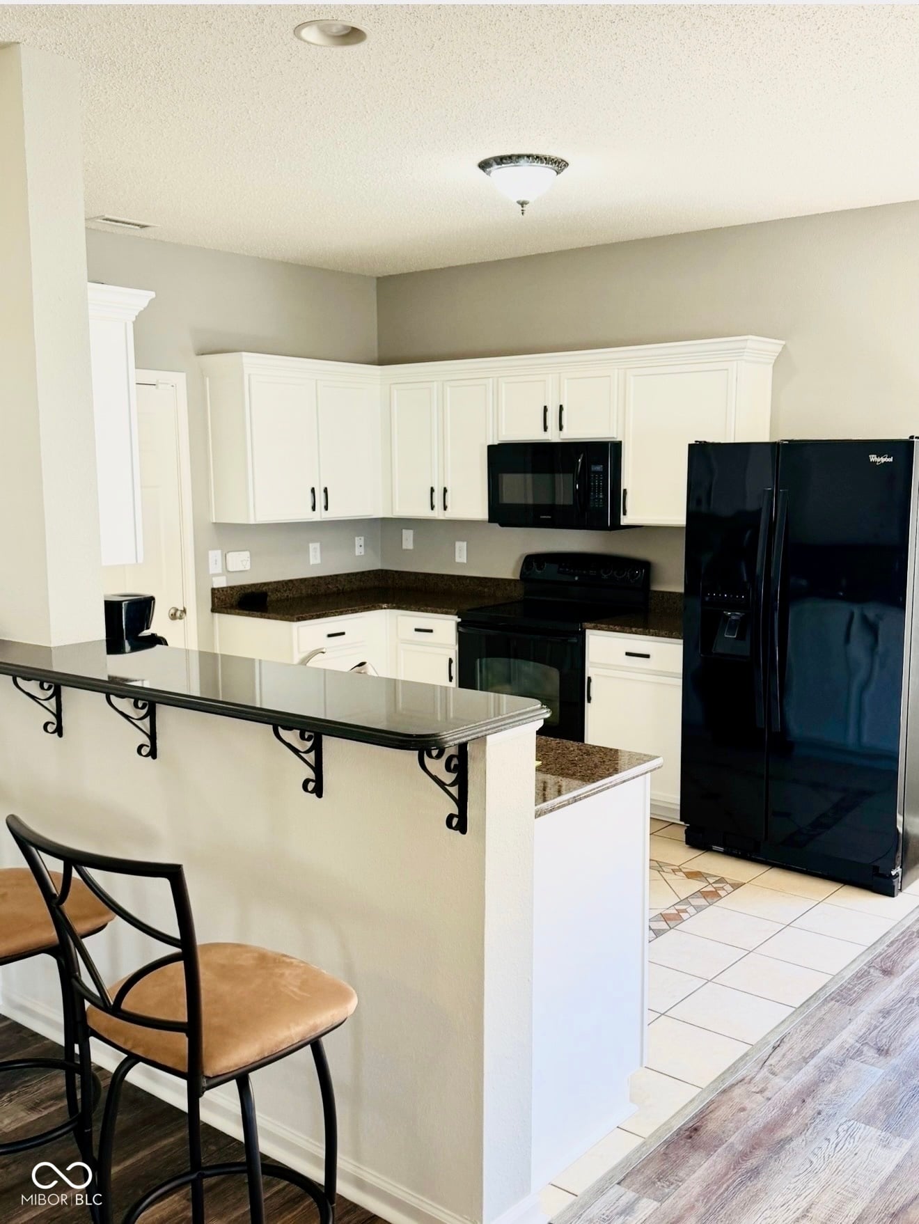 Modern white kitchen with black granite and island seating.