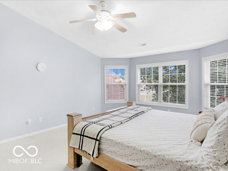 Bright primary bedroom with plantation shutters and multiple windows.