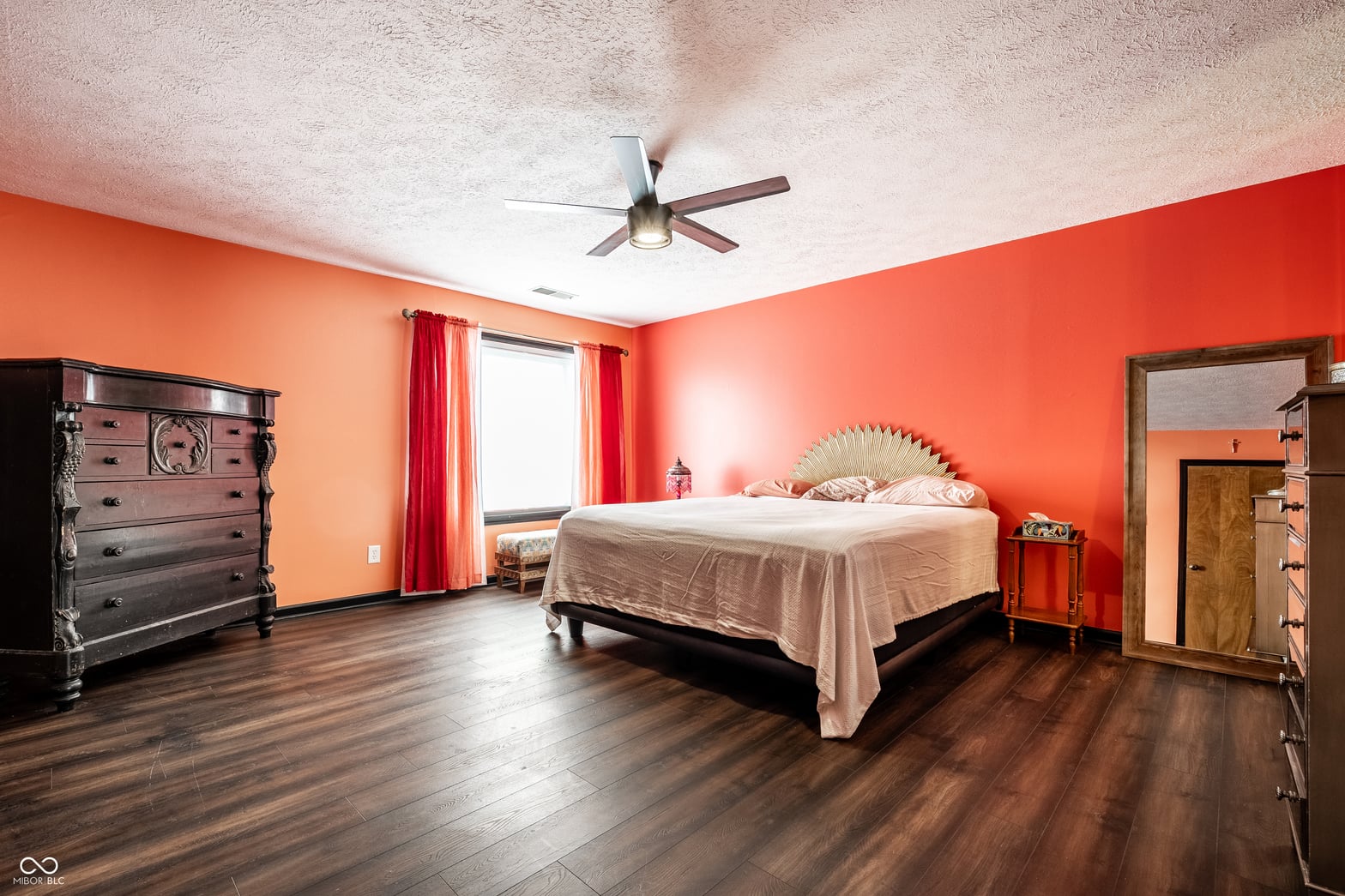 Spacious primary bedroom with vibrant walls and hardwood floors.