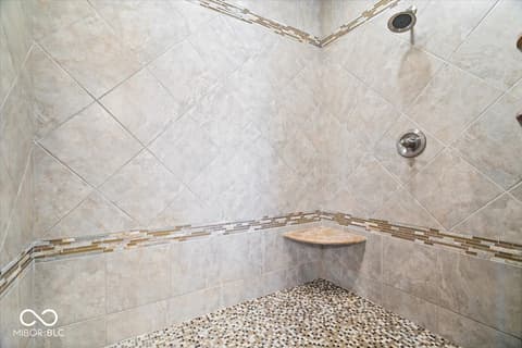 Primary bathroom at 16540 Shore Oaks Court, Noblesville, IN — Luxurious tile shower with marble and pebble details.