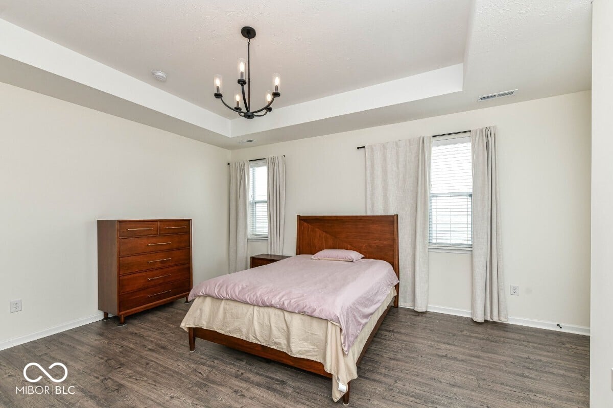 Bright primary bedroom with tray ceiling and ample windows.