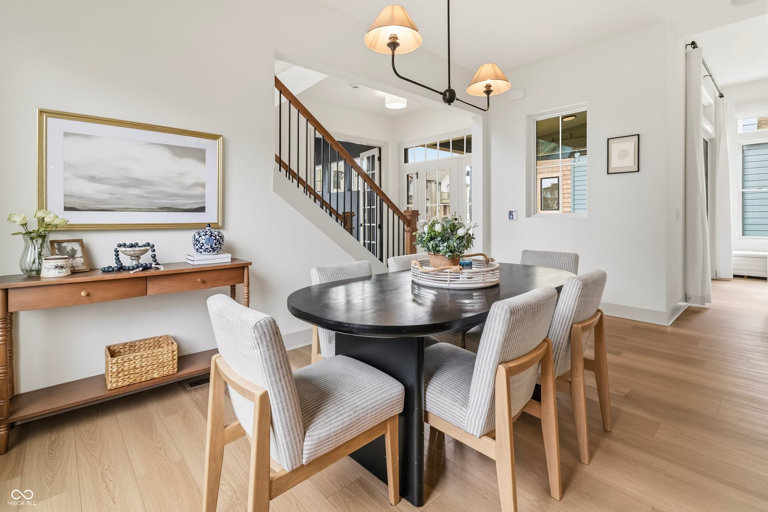 Bright open-concept dining with elegant black table and staircase.