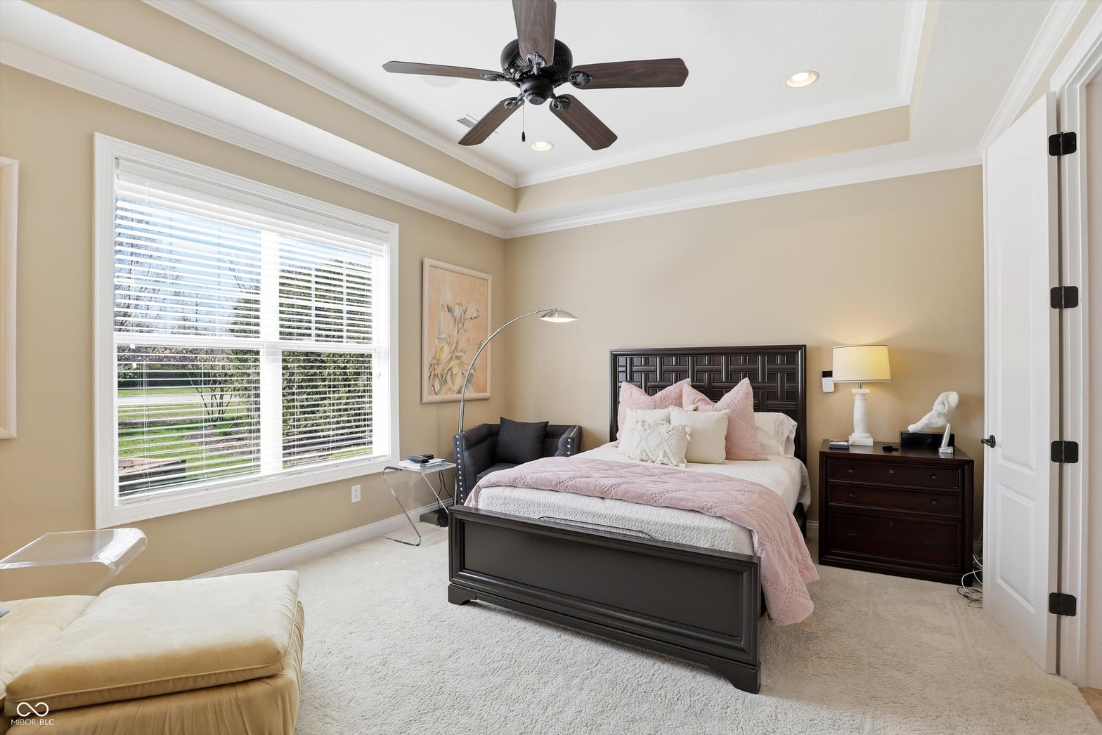 Bright primary bedroom with tray ceiling and plantation shutters.