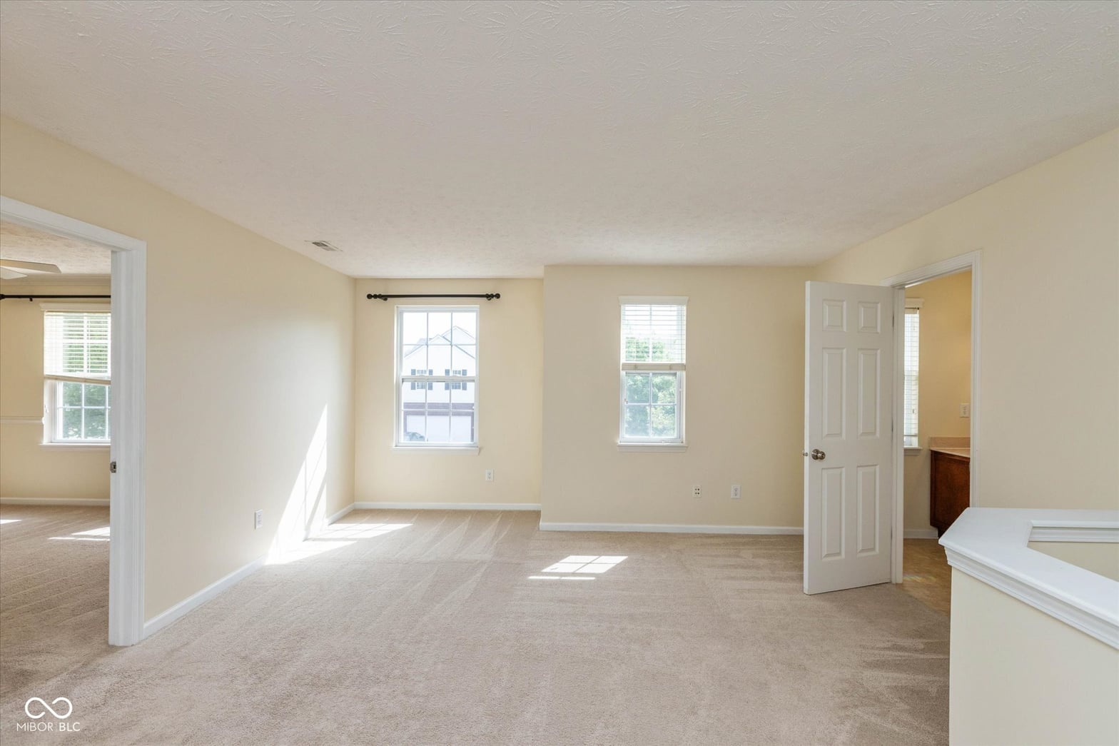 Bright primary bedroom with multiple windows and neutral decor.